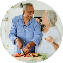 An older couple cutting vegetables, looking at each other and smiling